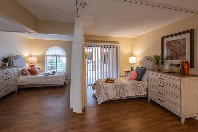 A cozy bedroom with two beds, natural lighting, and wooden flooring.