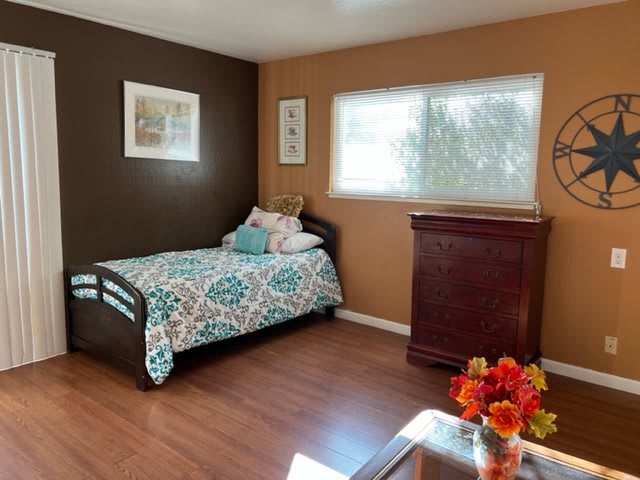 A cozy bedroom with a single bed, wooden flooring, and a chest of drawers near the window.