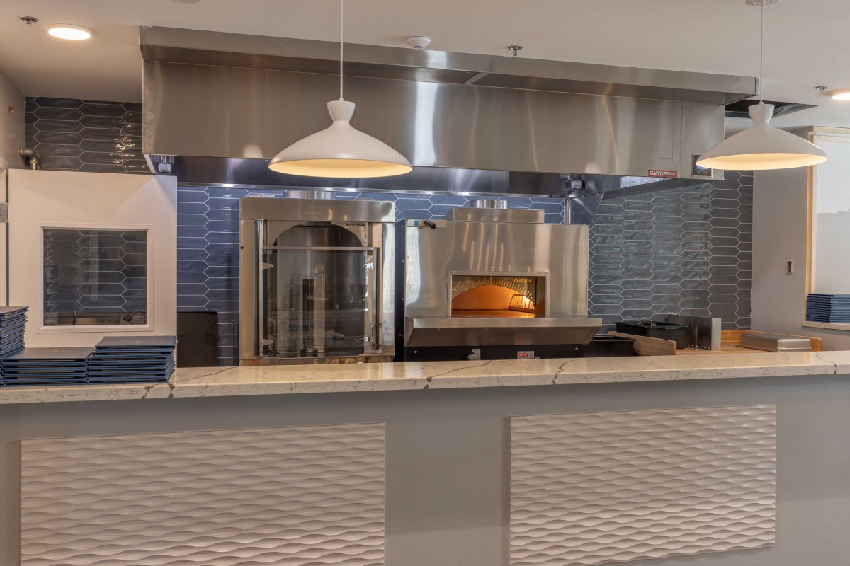 A modern restaurant kitchen featuring a wood-fired pizza oven and a tiled counter.