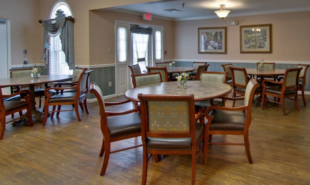 A spacious dining room with wooden tables and chairs, decorated with paintings and lit by a ceiling light.