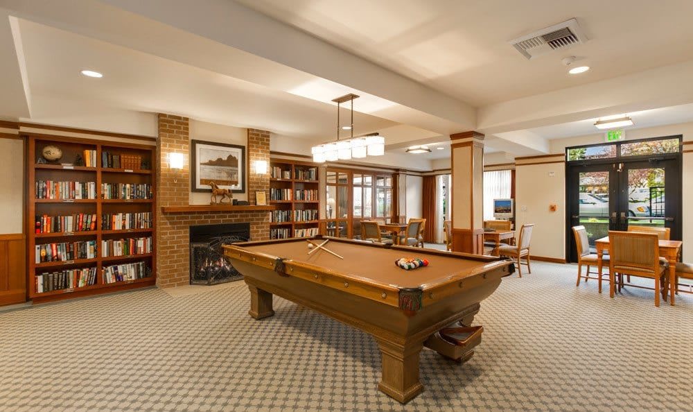 A cozy game room featuring a pool table and a library with bookshelves and a fireplace.
