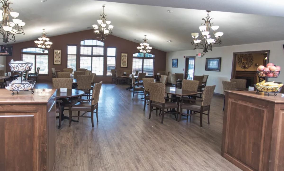 An empty dining room with wooden floors, chandeliers, and neatly arranged tables and chairs.