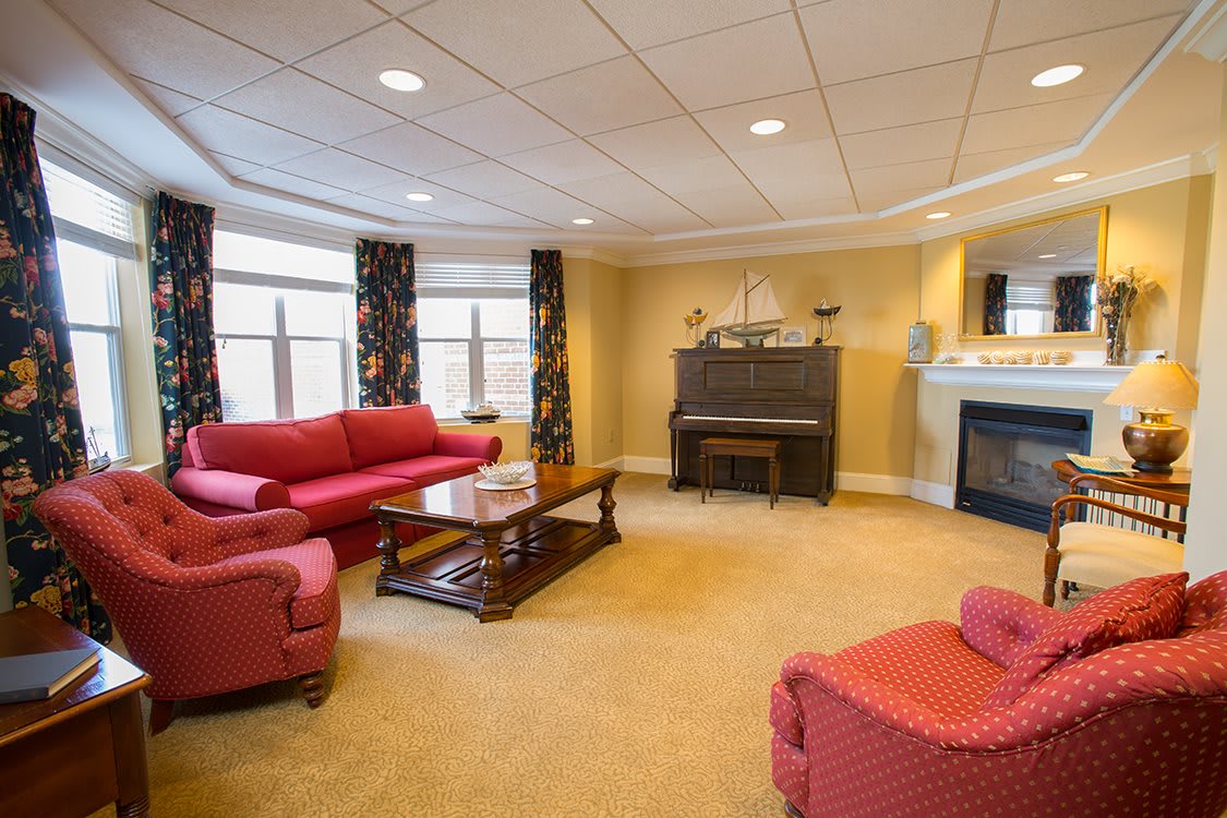 A cozy living room with a red sofa set, a piano, and a fireplace.