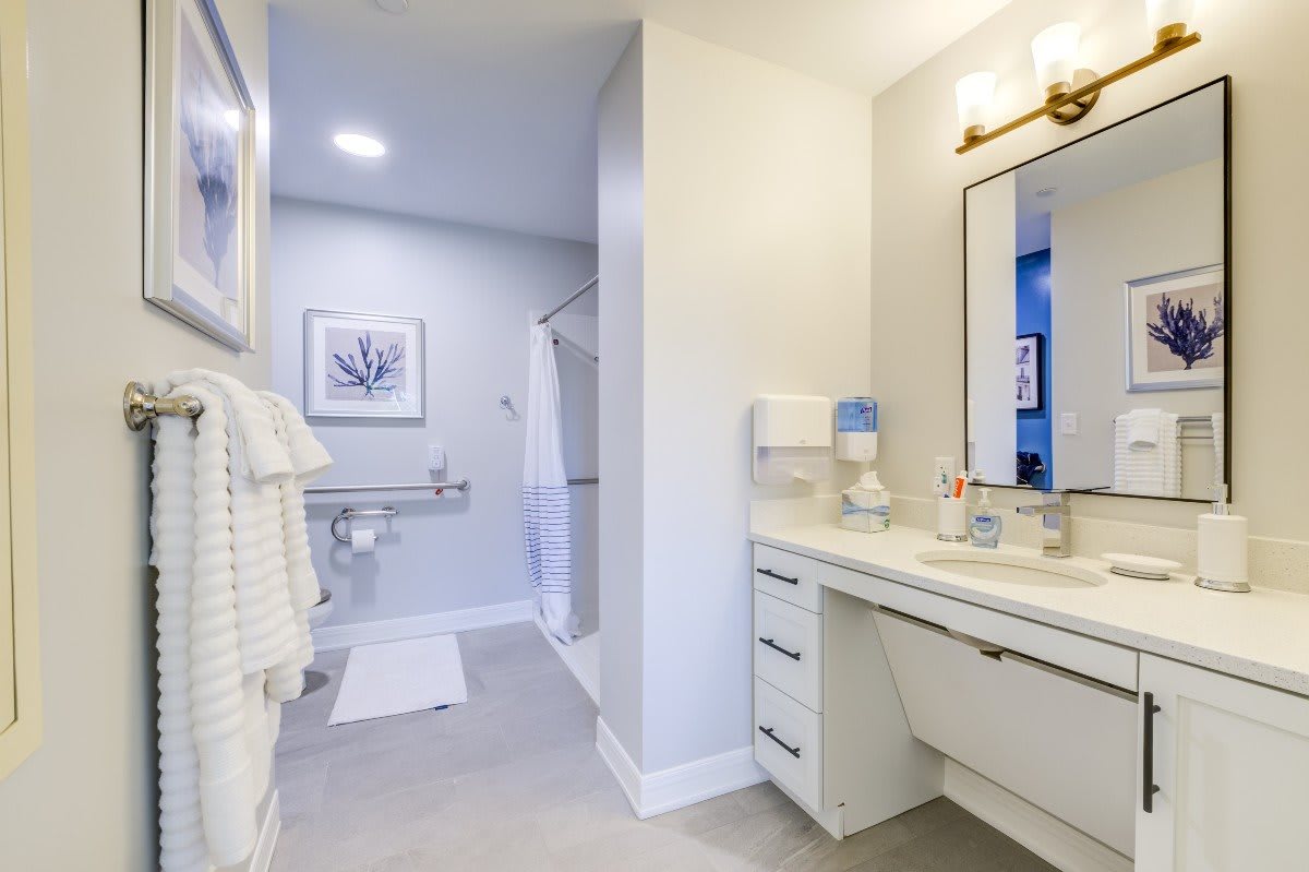 A modern and clean bathroom with white decor, featuring a mirror, sink, and neatly arranged towels.