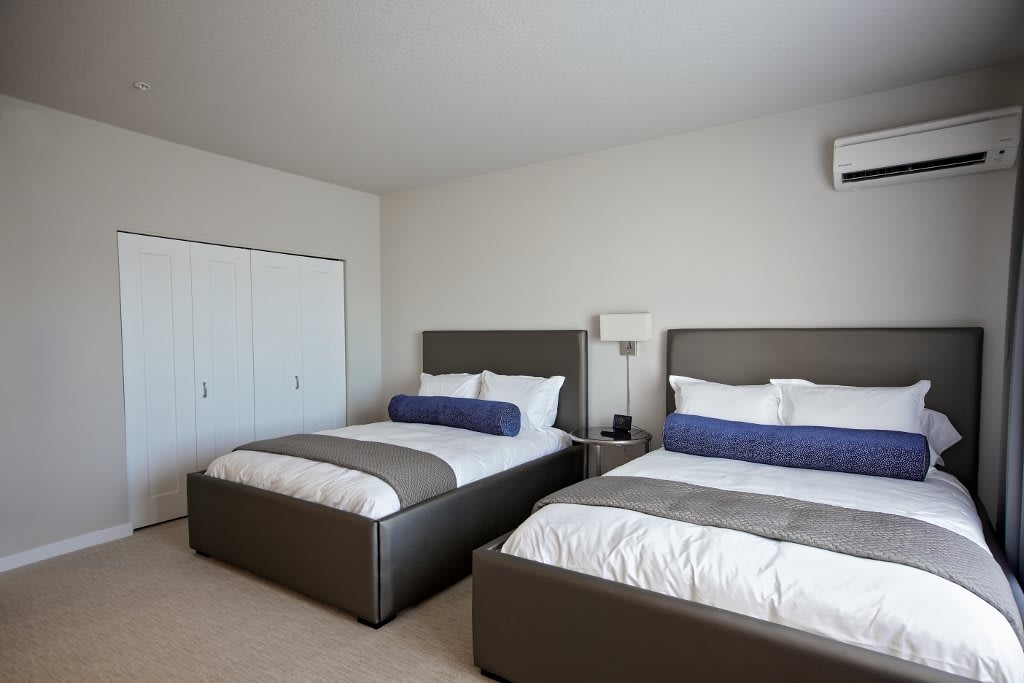 A modern bedroom featuring two neatly made beds with neutral tones and minimalist decor.