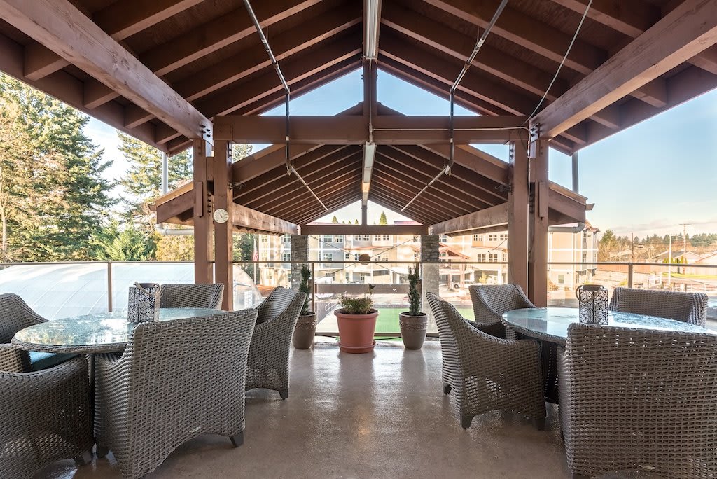 A spacious outdoor dining area with wicker furniture and a wooden roof.