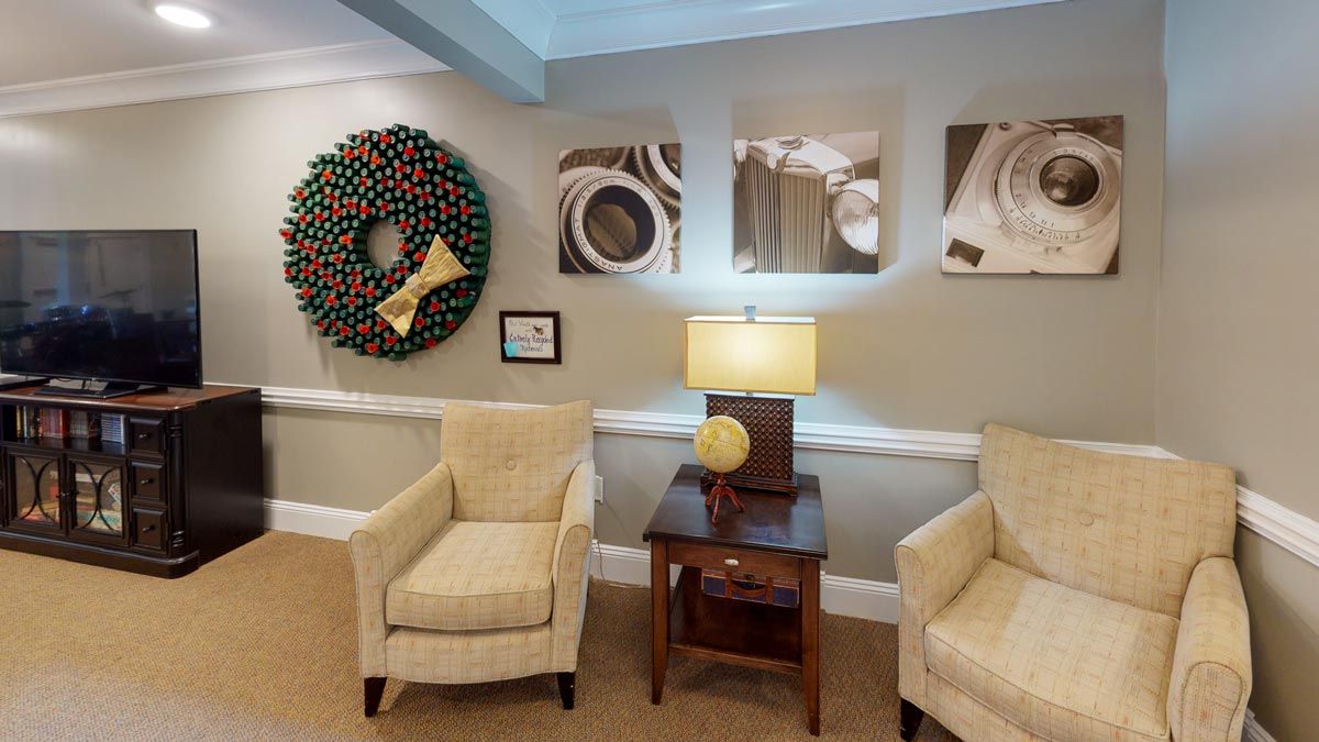A cozy living room with two beige chairs, a lamp, and decorative artwork on the walls.