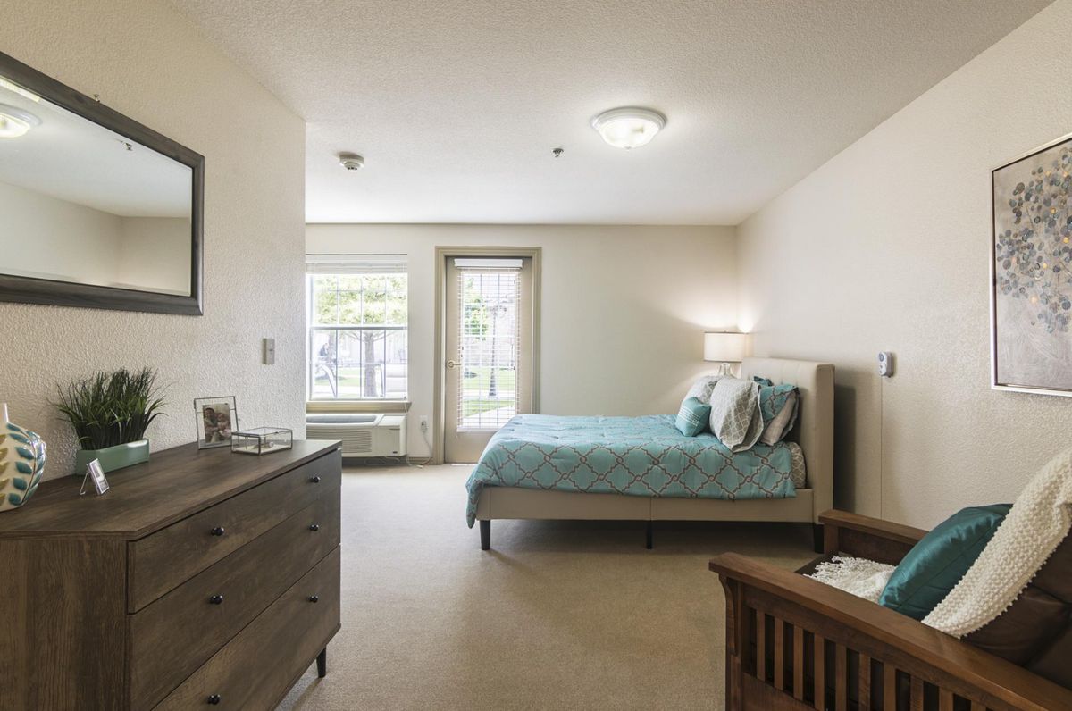 A spacious and well-lit bedroom featuring a comfortable bed, dresser, and large windows.