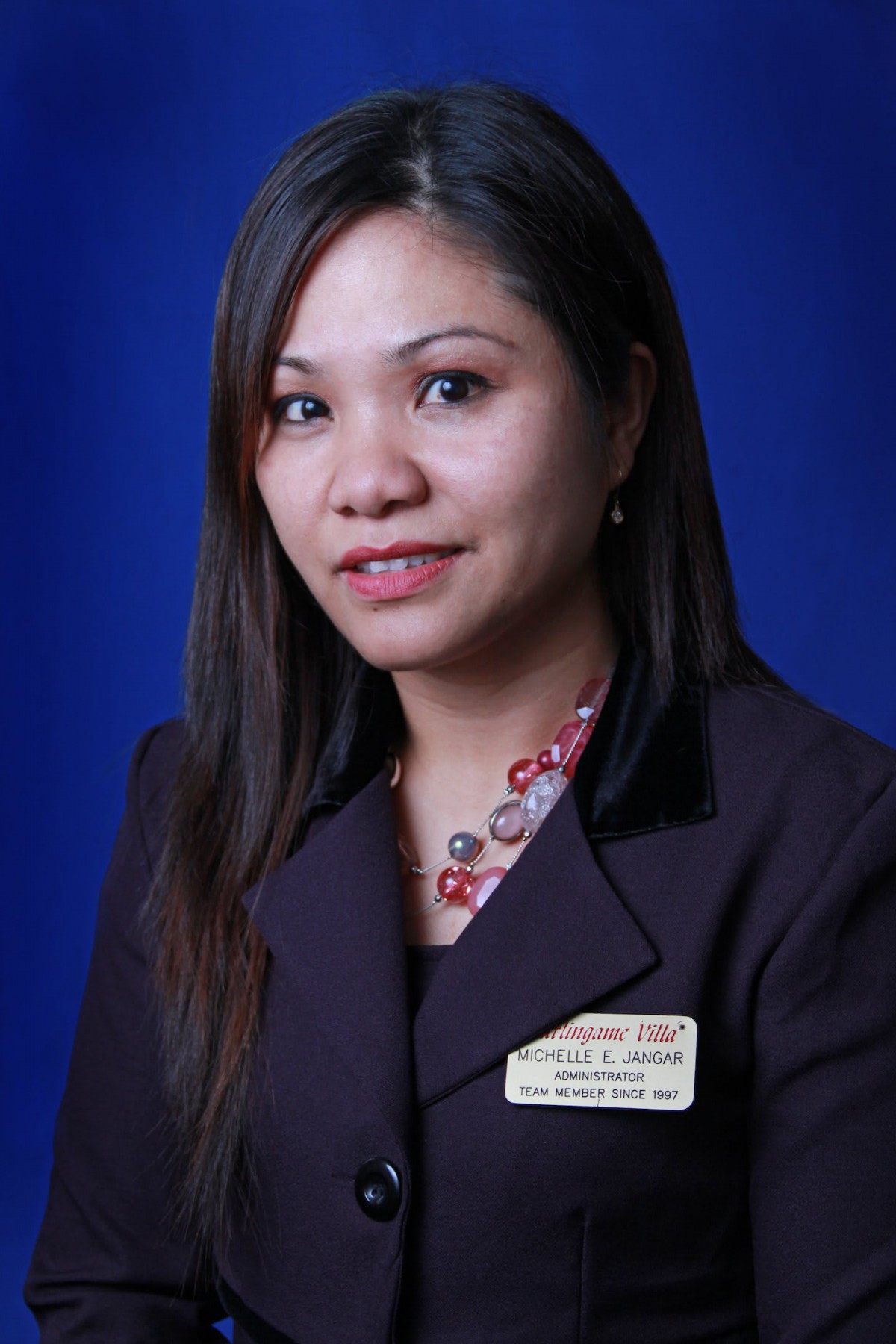 A professional portrait of a woman in business attire with dark hair against a blue background.