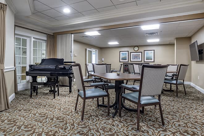A cozy, carpeted room with a grand piano and several tables and chairs arranged for seating.