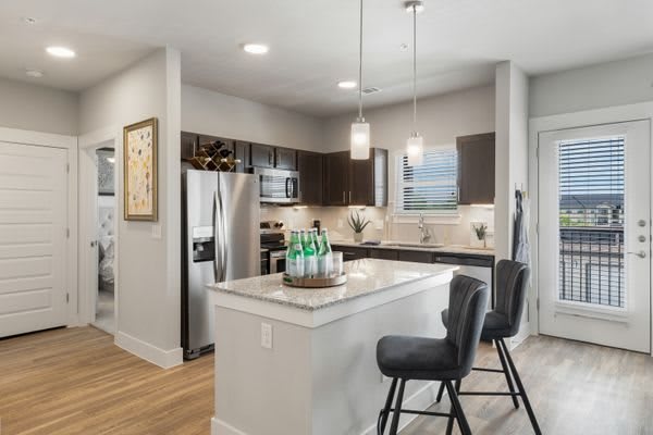 A modern kitchen with an island counter and stylish bar stools, featuring stainless steel appliances and elegant pendant lighting.