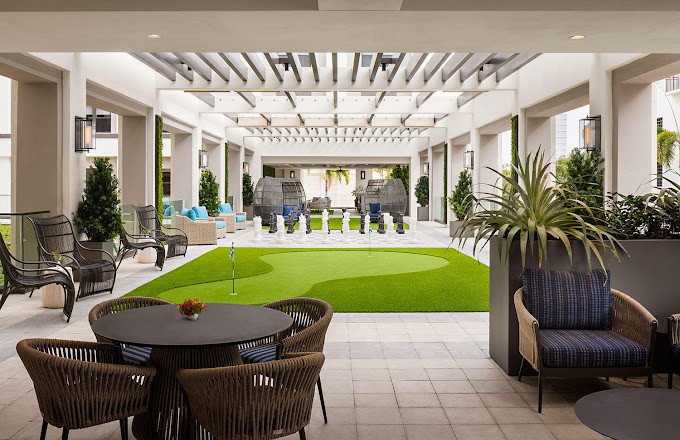 A modern indoor lounge area with seating and greenery, featuring artificial grass and stylish decor.