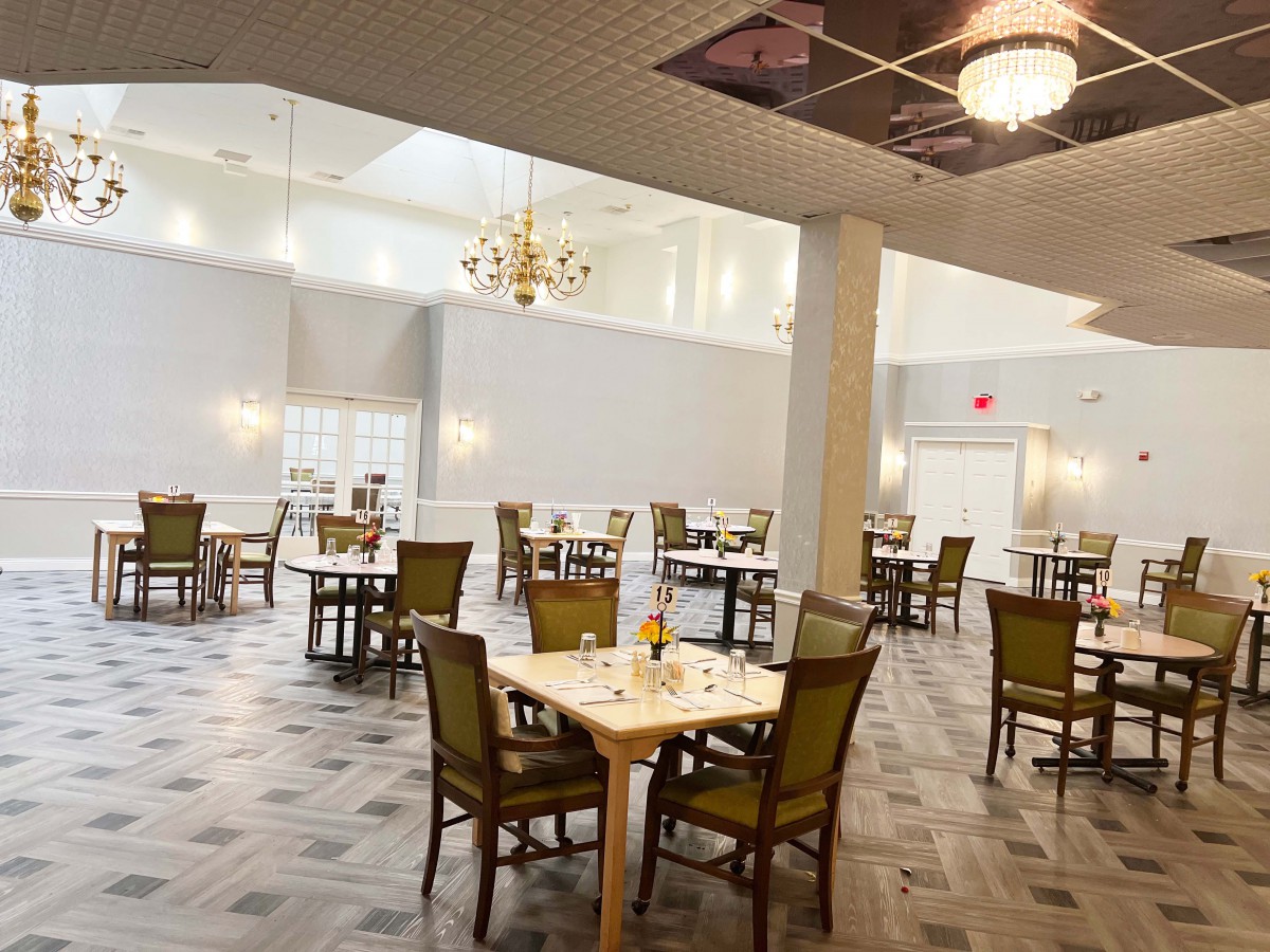 A spacious and elegantly designed dining area with several tables and chairs, lit by chandeliers.