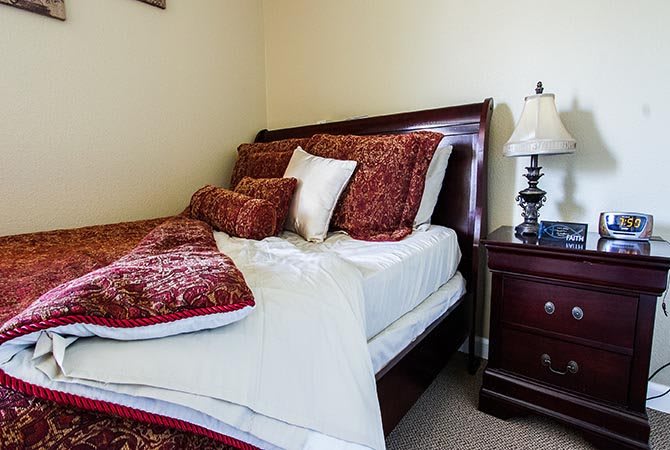 A neatly made bed with decorative pillows and a nightstand with a lamp in a cozy bedroom.
