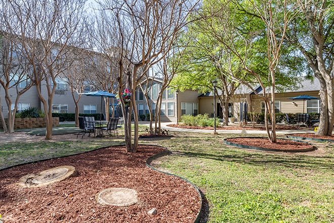 A well-maintained garden area in an apartment complex with trees and seating.