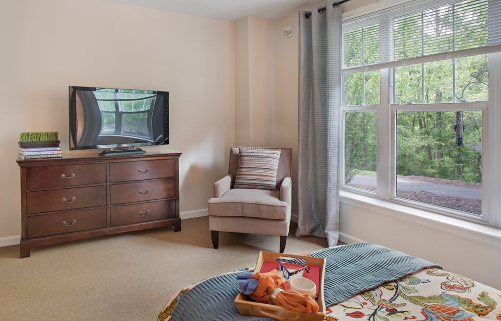 A cozy living room with a chair, television, and large window letting in natural light.