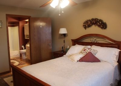 A cozy bedroom with wooden furniture, featuring a neatly made bed adorned with decorative pillows and a ceiling fan overhead.