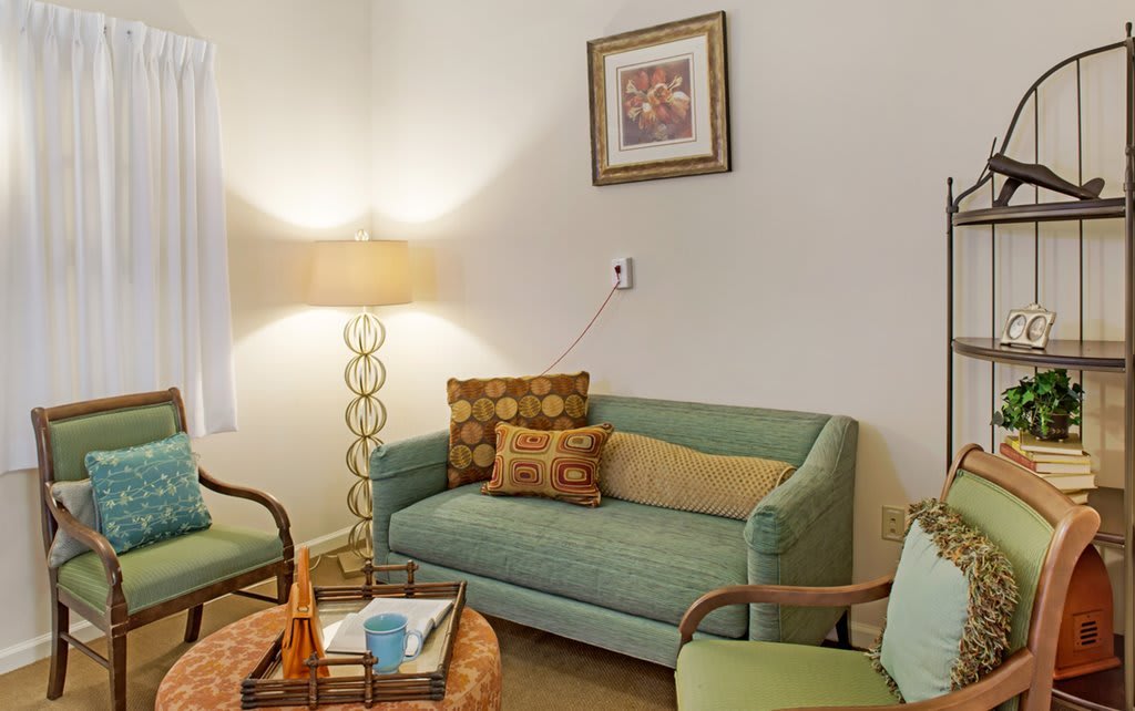 A cozy living room with a green sofa, patterned pillows, and a stylish lamp.