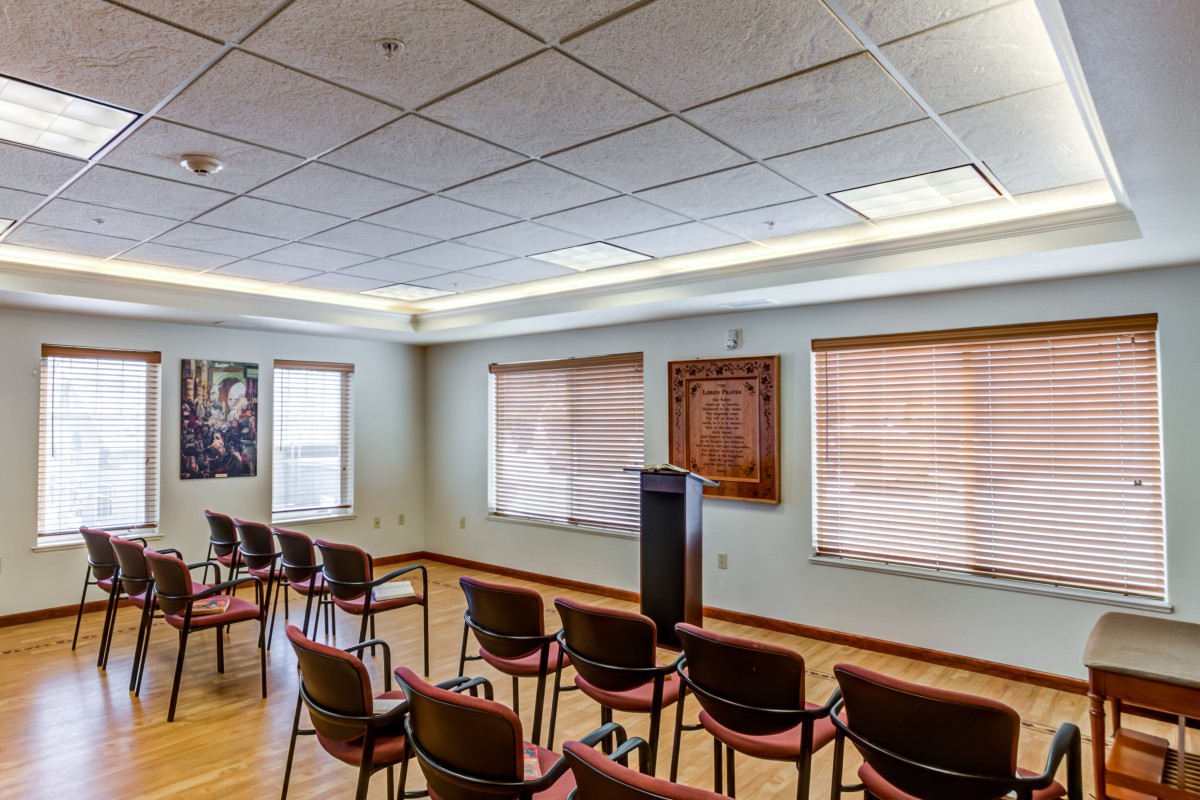 A small conference room with arranged chairs and a podium, featuring large windows and overhead lighting.