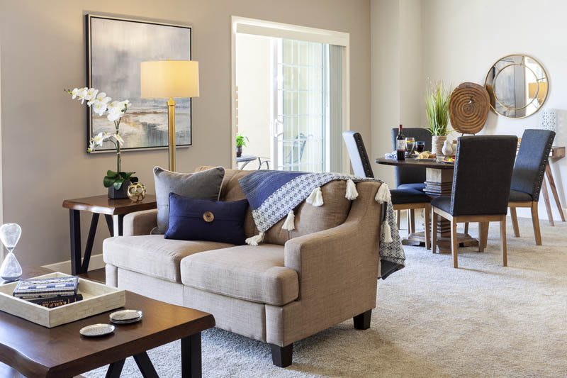 A cozy living room with a beige sofa, adorned with cushions and a throw blanket, adjacent to a dining area.