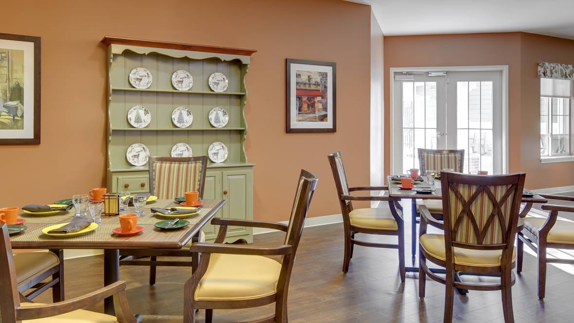 A cozy dining room with neatly arranged tables and chairs, featuring a decorative cabinet displaying plates.