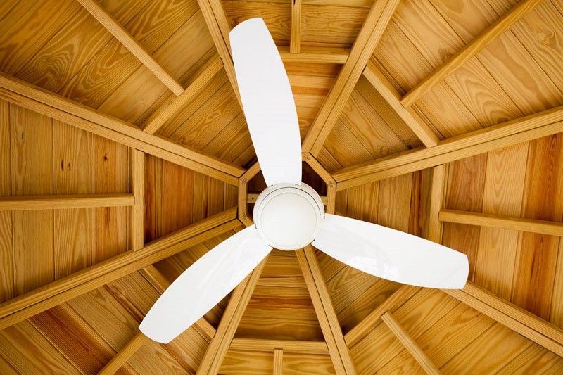 A white ceiling fan beneath a wooden paneled ceiling with geometric design.
