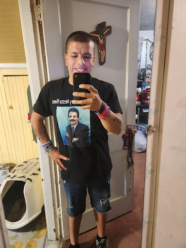 A man takes a selfie in front of a mirror, wearing a t-shirt with a graphic on it.