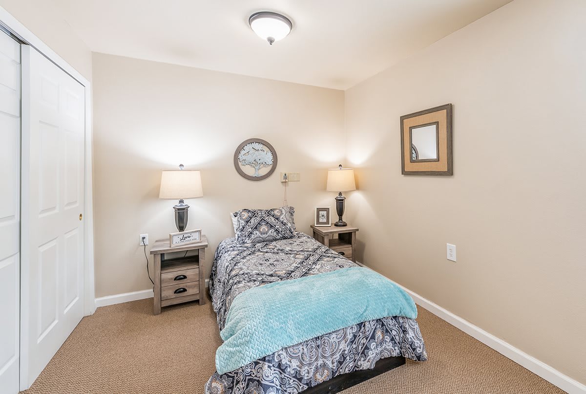 A cozy bedroom with a single bed adorned with a patterned comforter, flanked by two bedside tables and lamps. The walls are decorated with framed art.