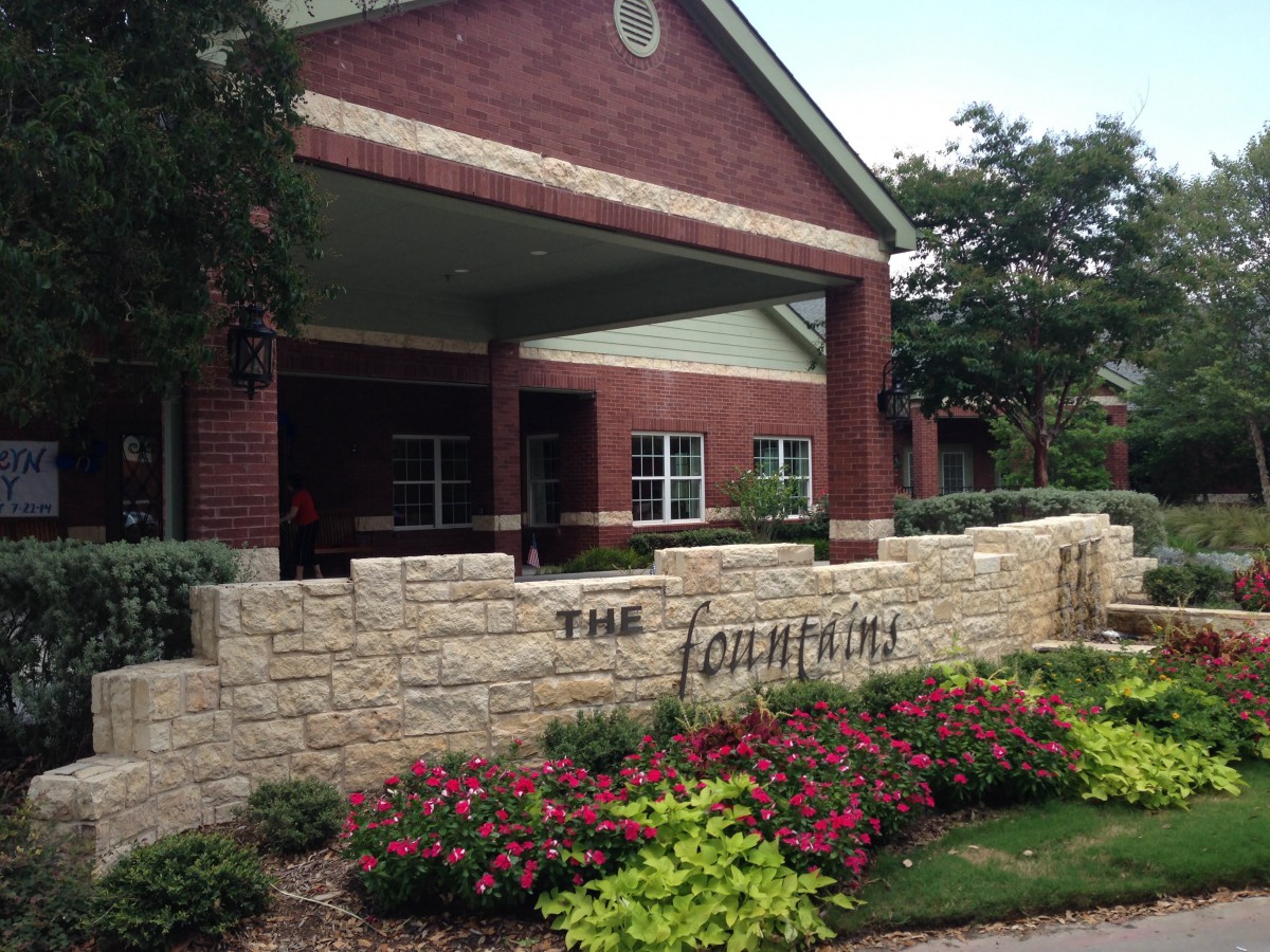 A residential building entrance with a landscaped garden and sign.