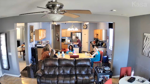 A cozy indoor gathering with people engaged in various activities around a dining table and kitchen.