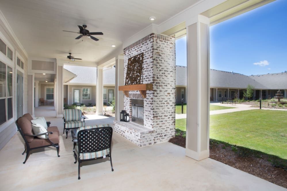 A spacious covered patio with a brick fireplace, ceiling fans, and outdoor furniture overlooking a garden.
