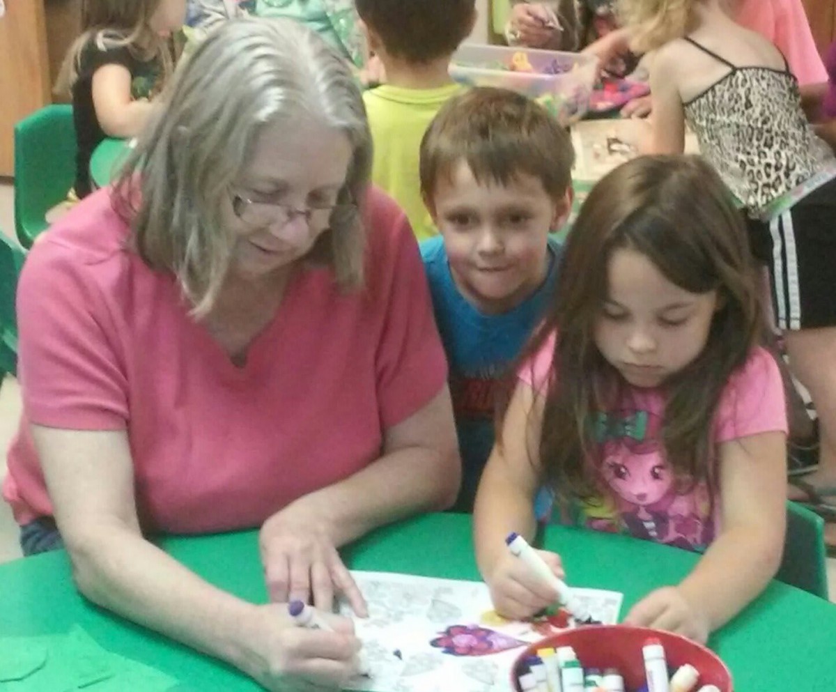 An adult helping two children with a drawing activity in a classroom setting.