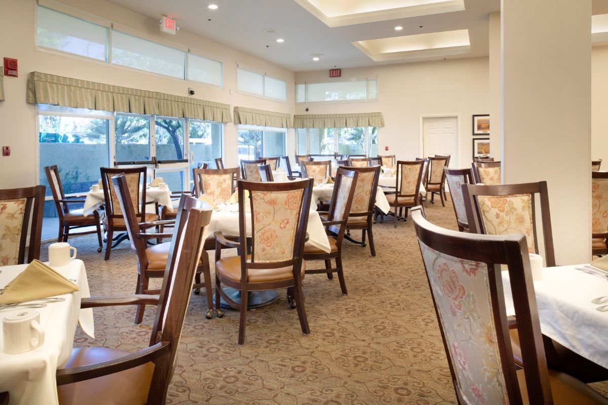 A spacious, elegantly furnished dining area with multiple tables and chairs, featuring large windows that allow natural light to brighten the room.