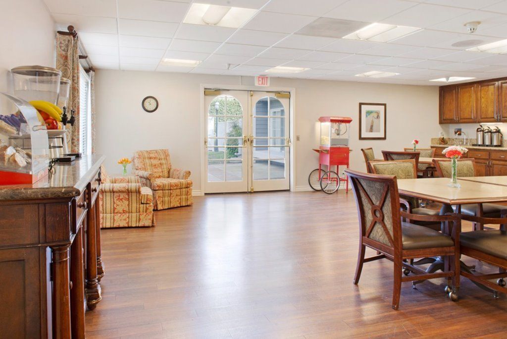 A spacious and well-lit room featuring wooden floors, comfortable seating, a round table, and a popcorn machine.