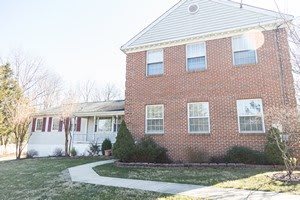 A suburban brick house with a front yard and pathway leading to the entrance.