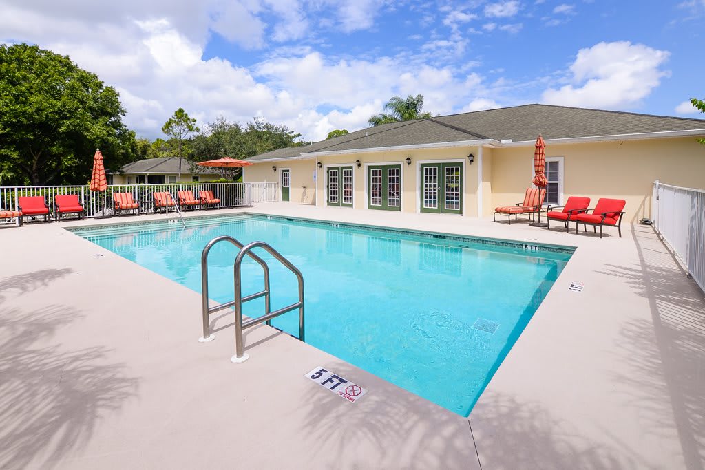 An outdoor swimming pool with poolside chairs and a residential building in the background on a sunny day.