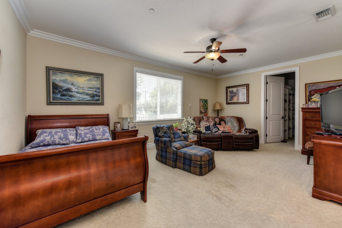 A spacious bedroom featuring a bed, sofa, ceiling fan, and wall artwork.