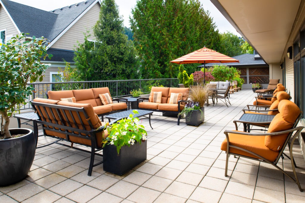 A spacious patio with comfortable seating and an outdoor umbrella, surrounded by greenery.