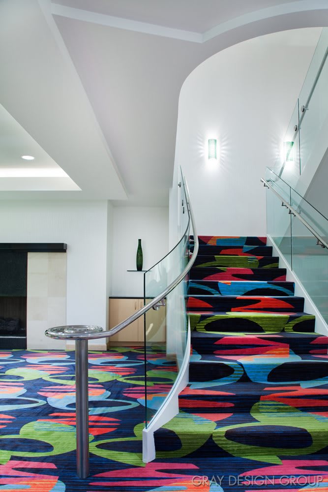 A modern hotel interior featuring a staircase with a vibrant, colorful carpet and glass railings.