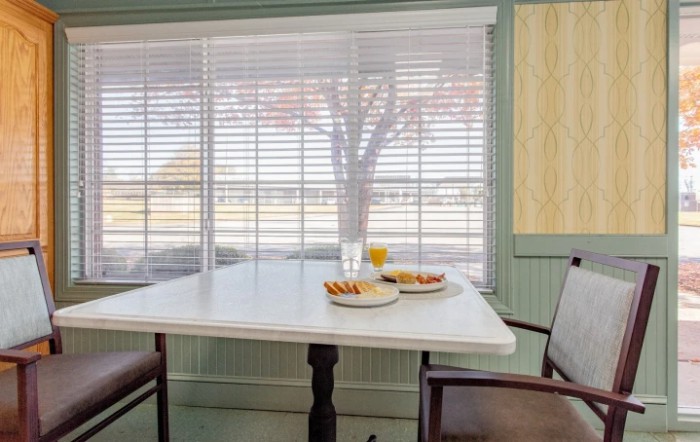 A cozy dining area with a table set for breakfast near a window with blinds.