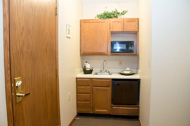 A compact kitchenette with wooden cabinets, a microwave, and a sink.