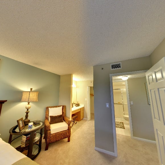 A cozy bedroom with a focus on a chair and side table next to a lamp, leading into an adjoining bathroom.
