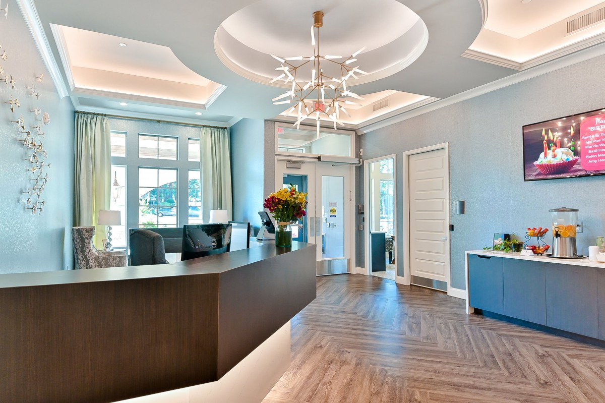 A modern reception area with a stylish chandelier, large windows, and a sleek desk.