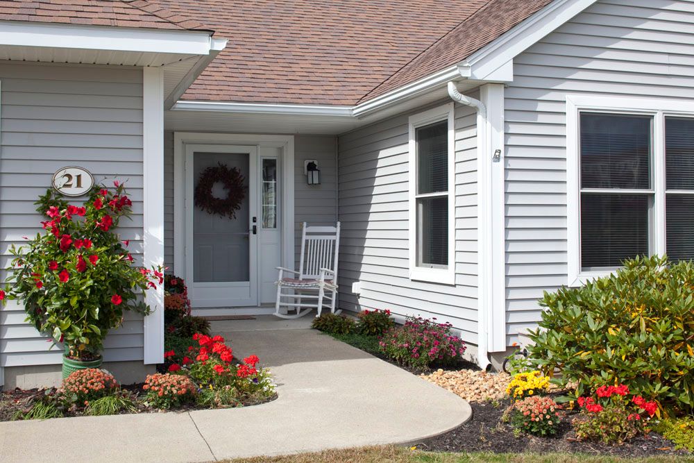 A welcoming front porch of a house with a rocking chair, flowers, and a wreath on the door.