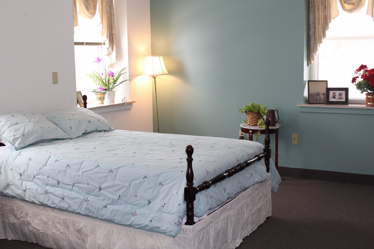 A cozy bedroom with a neatly made bed, a floor lamp, and a small plant by the window.