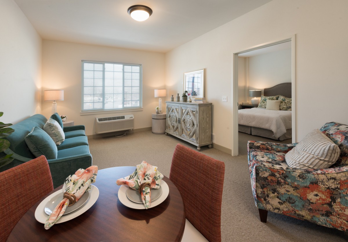 A cozy apartment living room with stylish furniture and decor, featuring a dining table, sofa, and a view into the bedroom.