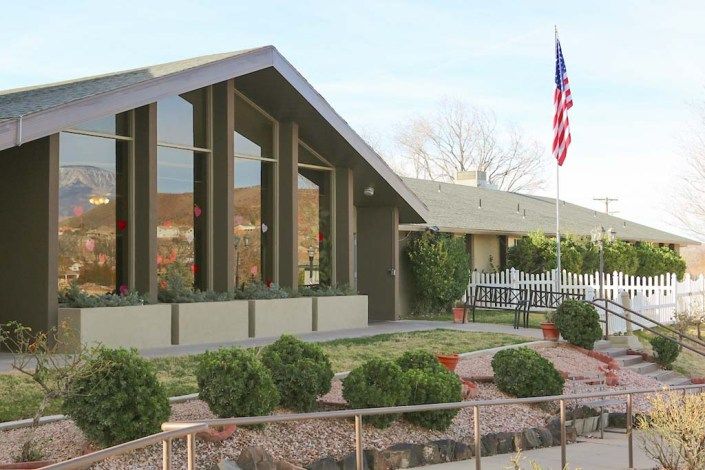 A mid-century modern house with large windows, an American flag, and neatly landscaped yard.