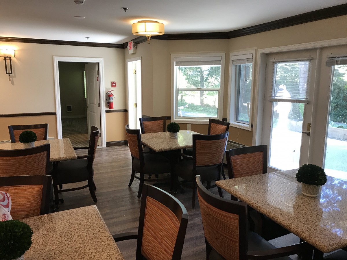 A cozy dining area with several tables and chairs, well-lit by natural daylight from the windows.