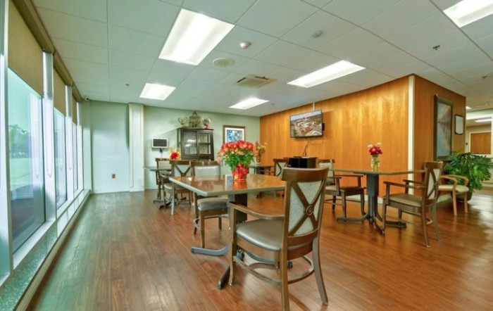 A modern dining area with wooden flooring, tables, and chairs adorned with flower arrangements.