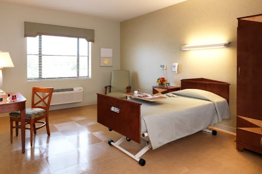 A well-lit patient room in a hospital, featuring a bed, chair, and window.